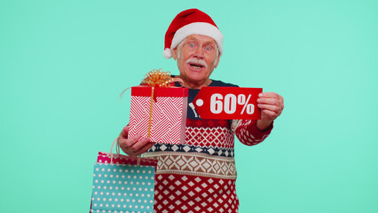 Grandfather man in Christmas sweater showing gift box and 60 Percent discount inscriptions banner text. Black Friday. Good holiday low prices for shopping. Blue studio wall background. Happy New Year