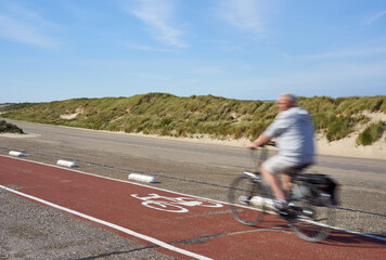 Bike path in the Netherlands. Track on a dam in front of the grass dunes. 1 man on bicycle motion blurred. Side view. Schouwen-Duiveland, Brouwersdam in South Holland.