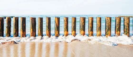 Foto op Plexiglas Wooden breakwater on the sandy shore, washed by the waves against the background of the sea © Denis Gavrilov Photo