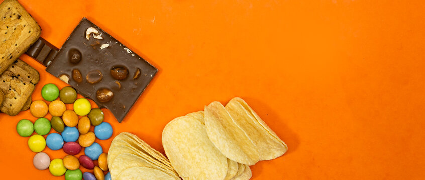 chocolate candy and bars and salt chips with cookies isolated on orange background