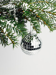 Christmas disco ball bauble hanging from pine tree branch against vibrant bright white background. Creative Xmas eve or New Year party celebration concept. Elegant winter holidays greeting card.