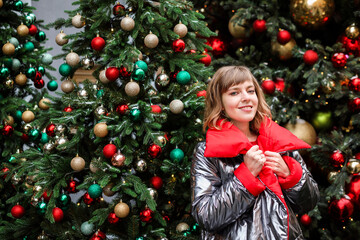 Portrait of attractive woman in silver and red coat among Christmas trees with festive decorations. 