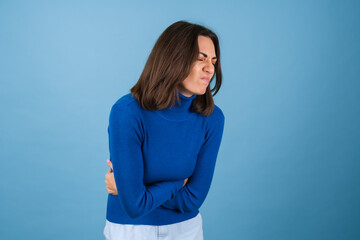 Young woman in golf on a blue background touches her stomach, suffers from pain during menstruation, indigestion