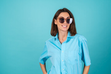 Young woman in a blue shirt on a background in sunglasses, fashionably stylish posing