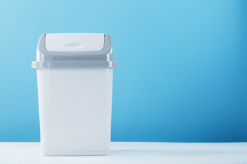 A white trash can with a lid on a blue background.