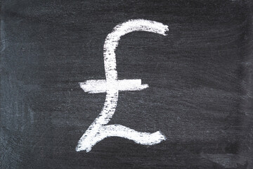 The symbol of the pound sterling on a black chalk board drawn in white chalk. Close up