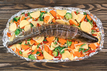 Fresh raw fish pike perch on foil for baking with vegetables, top view