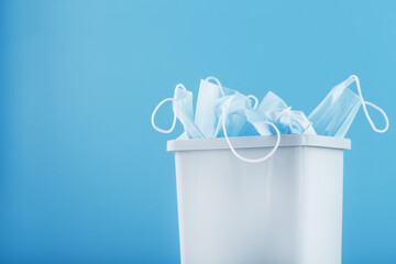 Waste bin full of used protective masks on a light blue background with free space.