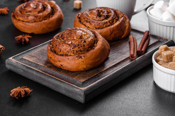 Freshly baked cinnamon roll with spices and cocoa filling on a black background