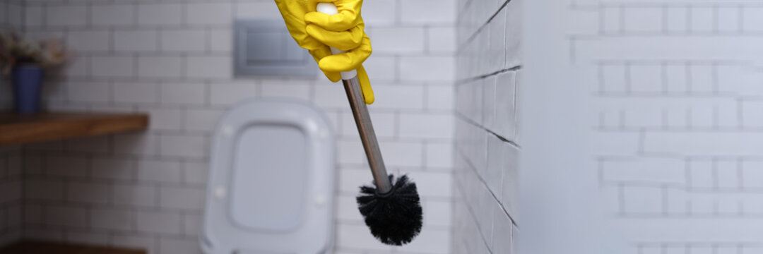 Cleaner in yellow rubber gloves holding toilet brush closeup