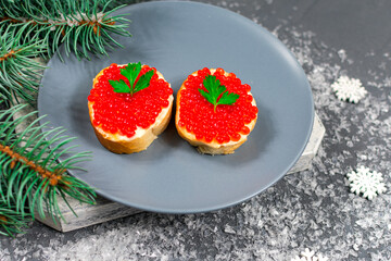 Sandwiches with red caviar on a gray plate on a table with branches of a Christmas tree and snowflakes. Christmas, New Years holidays. Festive food.