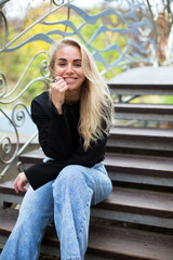 Obraz na płótnie Canvas beautiful caucasian blonde female in black sweater and jeans is sitting on the bridge stairs in the autumn park