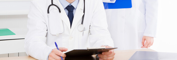 doctor posing in office with medical staff, he is wearing a stethoscope