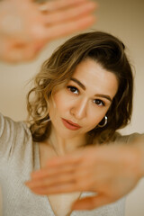 Fototapeta premium young caucaisan woman extends her arms out in front of her, beauty girl looks forward and puts her palms out, portrait of a young european lady at the beige wall, who puts her hands out in front of