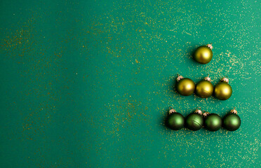Alternative green and yellow christmas balls make tree on jade green background with gold colored glitter. Christmas Holidays and present concept flat lay with copy space.