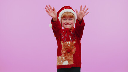 Girl in Christmas sweater waves hand palm in hello gesture welcomes someone with hospitable expression expresses positive emotions on violet studio background. Happy New Year holidays eve celebration