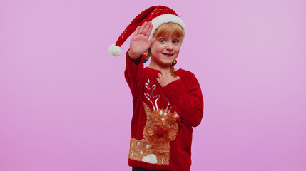 Girl in Christmas sweater waves hand palm in hello gesture welcomes someone with hospitable expression expresses positive emotions on violet wall background. Happy New Year holidays eve celebration