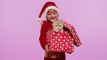 Toddler girl in Christmas Santa sweater smiling, unwrapping gift, opening box with pet cat, expressing great surprise. Little child kid indoors studio isolated on violet background. Happy New Year