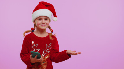 Girl in Christmas Santa hat with mobile phone showing pointing empty place, advertising area for commercial text, copy space for goods promotion on violet background studio. Happy New Year shopping