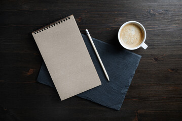 Blank kraft notebook, pencil and coffee cup on stone board. Copy space. Flat lay.