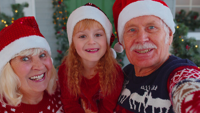 POV Shot Of Senior Couple Grandparents With Grandchild Girl Kid Taking Selfie On Mobile Phone Near Decorating Christmas House Celebrating New Year Eve. Family Enjoying Holidays Time Together At Home