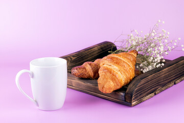 White mug on pink background with wooden tray and croissant.