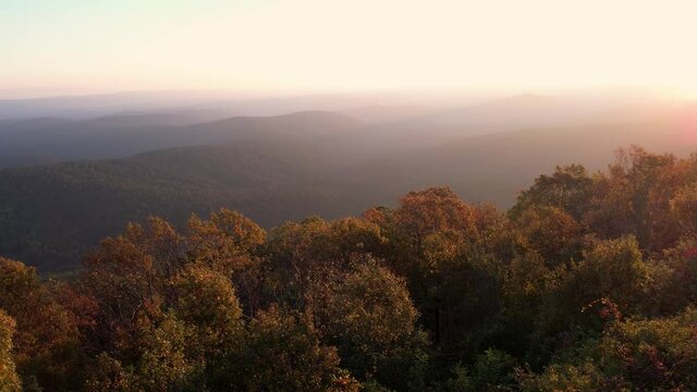 Slow pan across the view of sun rising just over scenic mountaintop in Ouachita National Forest, with November fall colors, mist in valleys