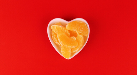 Slices of tangerine in a plate in the shape of a heart on a red background