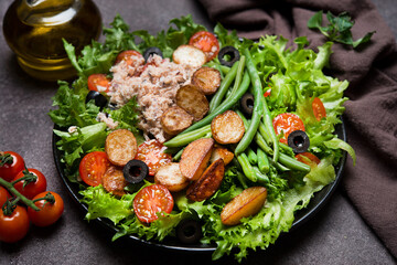 Nicoise salad with tuna, tomatoes, potatoes and green beans on a dark background