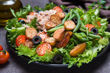 Nicoise salad with tuna, tomatoes, potatoes and green beans on a dark background