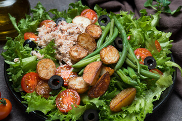 Nicoise salad with tuna, tomatoes, potatoes and green beans on a dark background