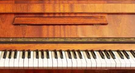 Front view of a brown old piano. White keys and brown piano
