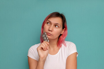 Fototapeta premium picture of thoughtful young woman with pills on a blue background