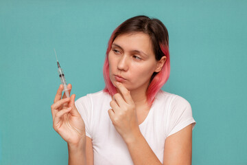 A young woman holds a syringe in her hands, wondering whether to get vaccinated against coronavirus