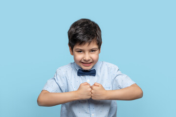 Waist up portrait of a little boy in a fighting mood against  blue background in the studio © rozaivn58