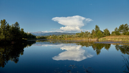 A strange cloud is reflected in the water of a lake. The lake is located in Gorj, Romania.
