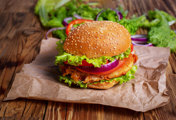 Burger with meat, onions and green salad on a wooden table