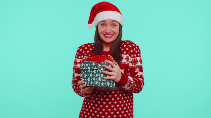 Cheerful teen girl 20s in red Christmas Santa deer sweater getting present gift box, expressing amazement, extreme happiness isolated on blue background. Happy New Year celebration merry holidays