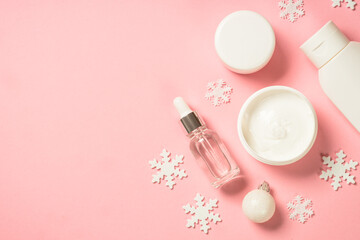 Winter cosmetic, skin care product. Cream, serum, tonic with winter decorations. Top view on pink background with copy space.