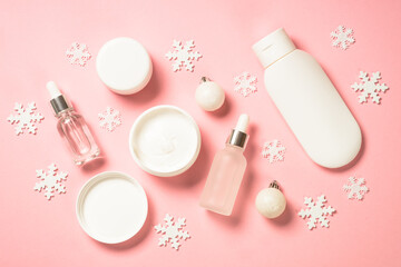 Winter cosmetic, skincare product. Cream, serum, tonic with winter decorations. Top view on pink background with christmas decorations.