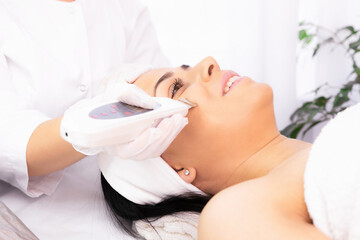 Fototapeta na wymiar Happy woman, female client getting procedure facial ultrasound cavitation by a cosmetologist in a beauty salon, facial peeling concept.