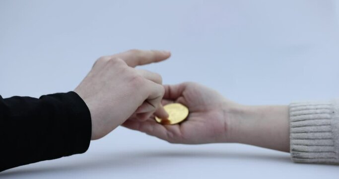 Male hand puts a cryptocoin, Bitcoin or BTC, in a woman's hand, depicting earning or paying with crypto or cryptocurrency and saving, holding or hodling. High quality 4k footage