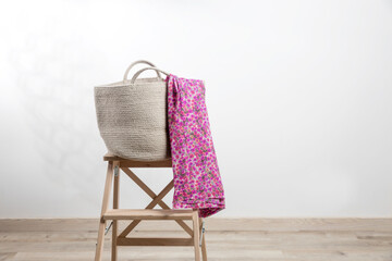 Large gray beach bag with a pink pareo woven from canvas on a beige stool against a white wall....
