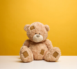 cute brown teddy bear with patches sits on a yellow background, childrens toy