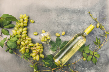 Top view of bottle white wine, green vine, wineglass and ripe grape on vintage gray stone table...