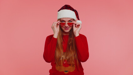 Adult girl 20s in red sweater Santa Christmas hat listening music dancing fooling around having fun expressive gesticulating hands isolated on pink wall background studio. Happy New Year merry holiday