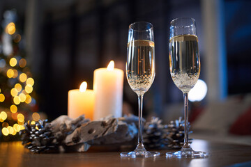 Two glasses of champagne standing on table with christmas tree on background. Candles as decoration around. Concept of winter holidays.