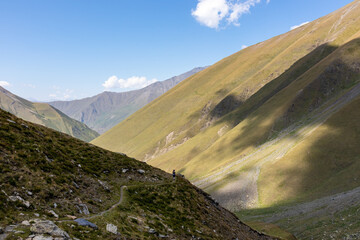 A female backpacker on a hiking trail with a panoramic view on the green hills and sharp ridges of the mountain peaks in the Greater Caucasus Mountain Range in Georgia, Kazbegi Region. Wanderlust.