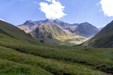 A panoramic view on the high mountain peaks of the Chaukhi massif in the Greater Caucasus Mountain Range in Georgia, Kazbegi Region. A valley with lush green pastures. Wanderlust. Remote location.