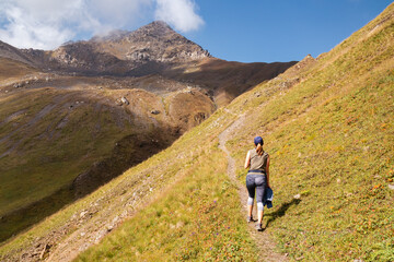 Fototapeta premium A woman on a hiking trail with a panoramic view on the Chaukhi Pass and its mountain peaks in the Greater Caucasus Mountain Range in Georgia, Kazbegi. The valley is lush green. Wanderlust.